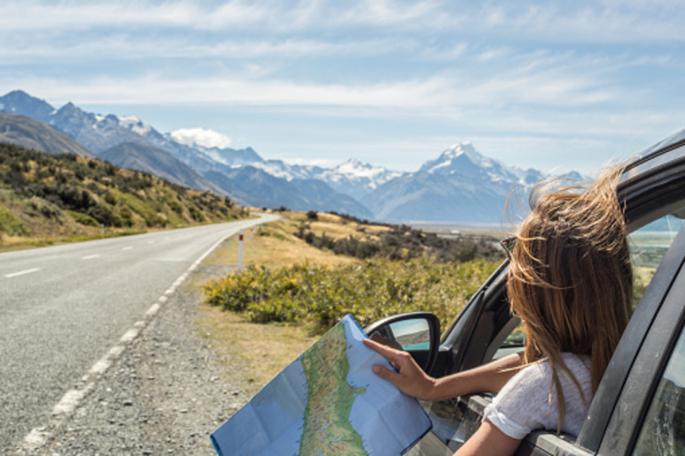 young girl with map leaning out of the car on holiday